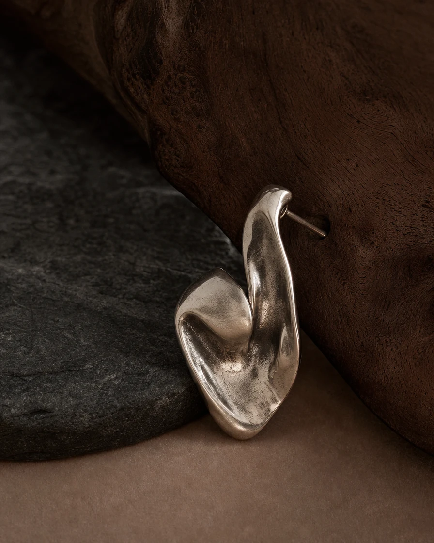 Sculptural silver jewellery resting on walnut and charcoal stone